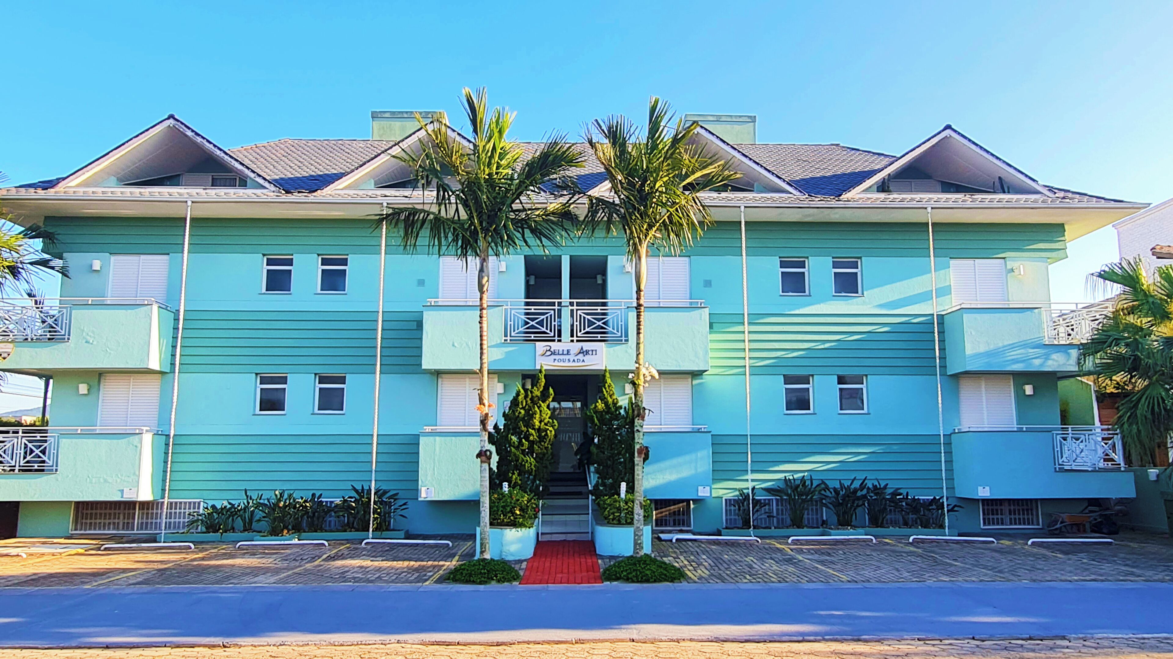A multi-story hotel with a blue facade, a central entrance with a red carpet, and palm trees in front.