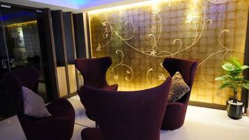 Um lobby moderno com poltronas roxas escuras, uma parede decorativa com padrões abstratos e uma planta em vaso.