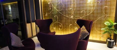 A modern lobby with dark purple armchairs, a decorative wall with abstract patterns, and a potted plant.