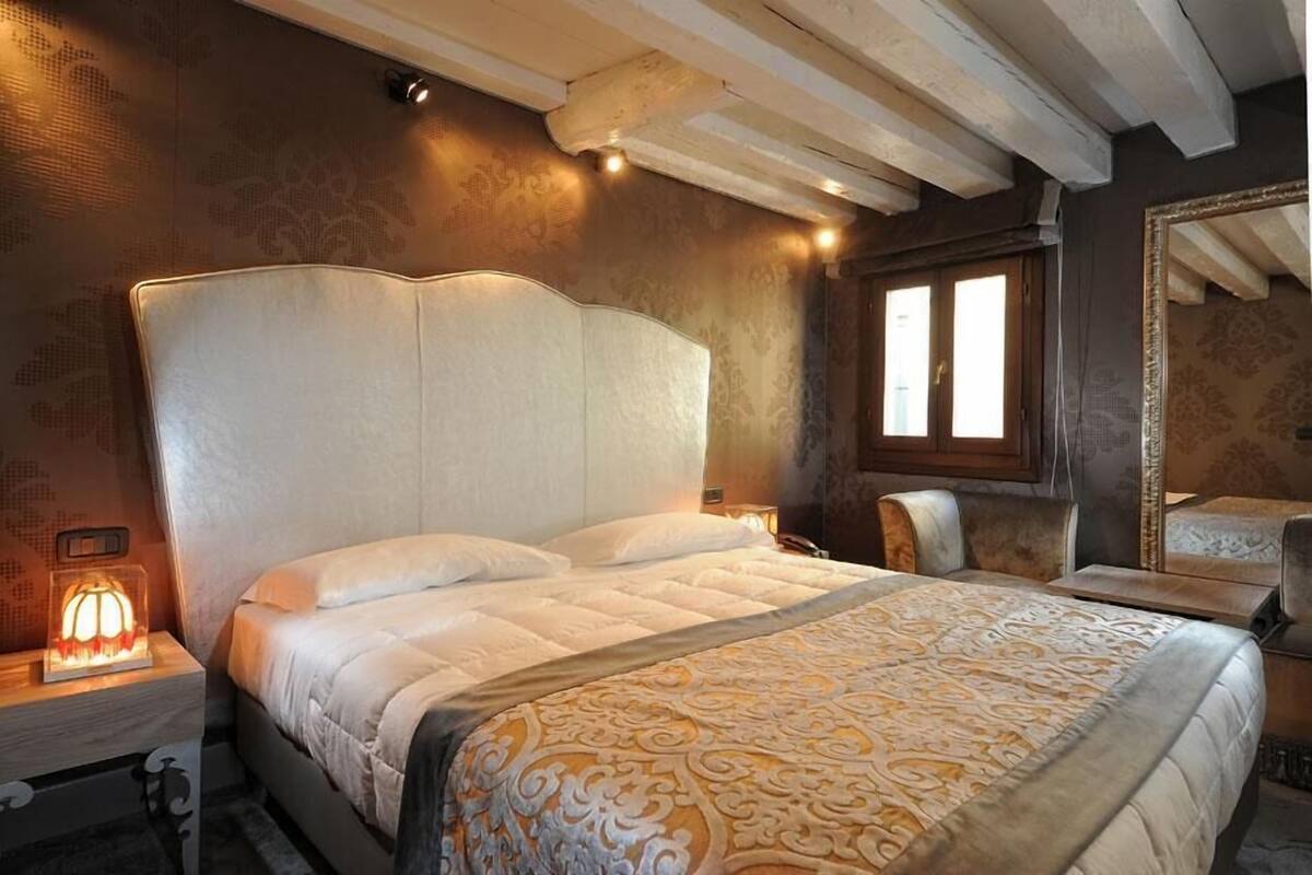 A bedroom with a large bed, a bedside table with a lamp, and a mirror on the wall.