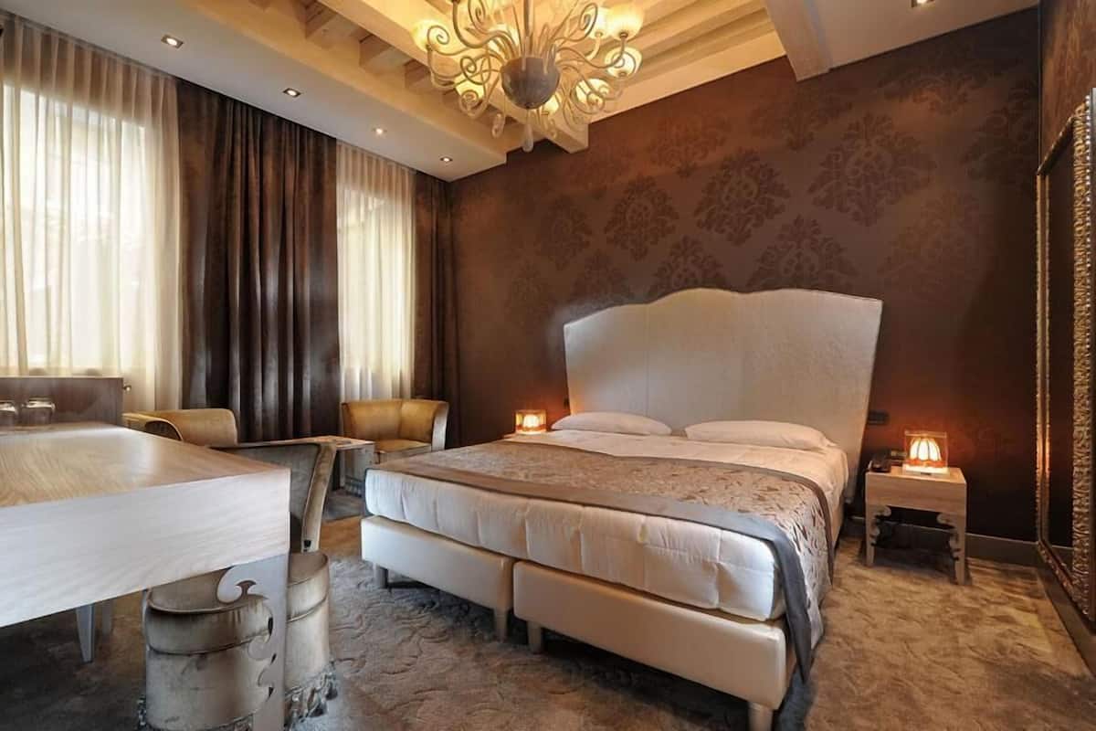 A spacious bedroom with a large bed, a bedside table, a nightstand, and a desk with a chair.