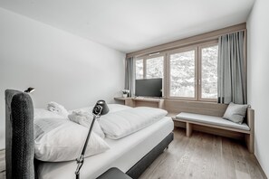 A modern bedroom with a bed, bedside table, TV, and a window with curtains.
