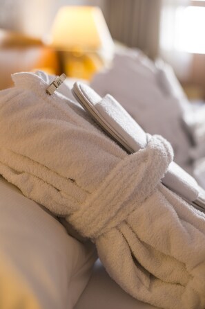 Una cama bien hecha con sábanas blancas y una bata blanca colgada.