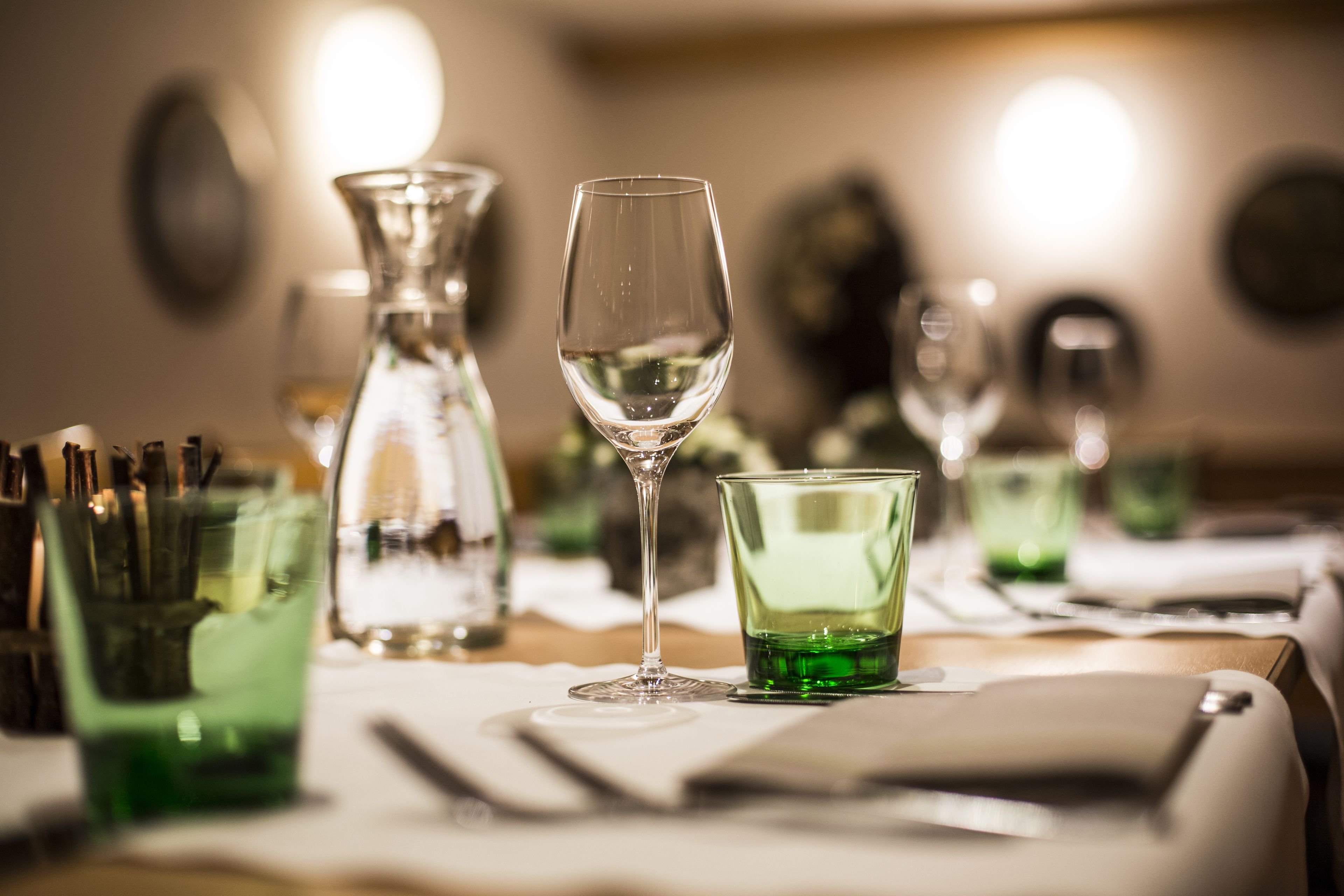 Una mesa de comedor con vasos de vidrio verde y una copa de vino transparente.