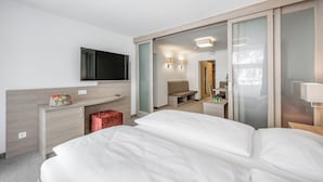 A modern hotel room with a large bed, a desk with a flat-screen TV, a seating area, and a sliding door leading to a bathroom. - all inclusive Hotel Lohmann (Soelden)