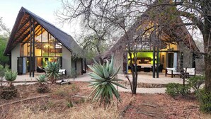 A modern two-story house with a sloped roof, large glass windows, and a patio area with outdoor furniture.