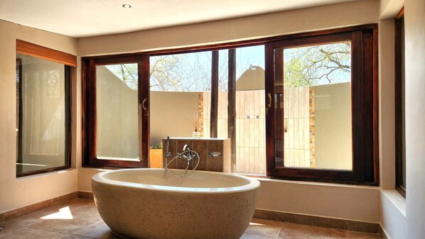 A bathroom with a freestanding bathtub, large windows, and a view of a backyard.