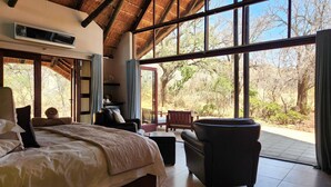 A bedroom with a large bed, a chair, a table, and a view of the outdoors.