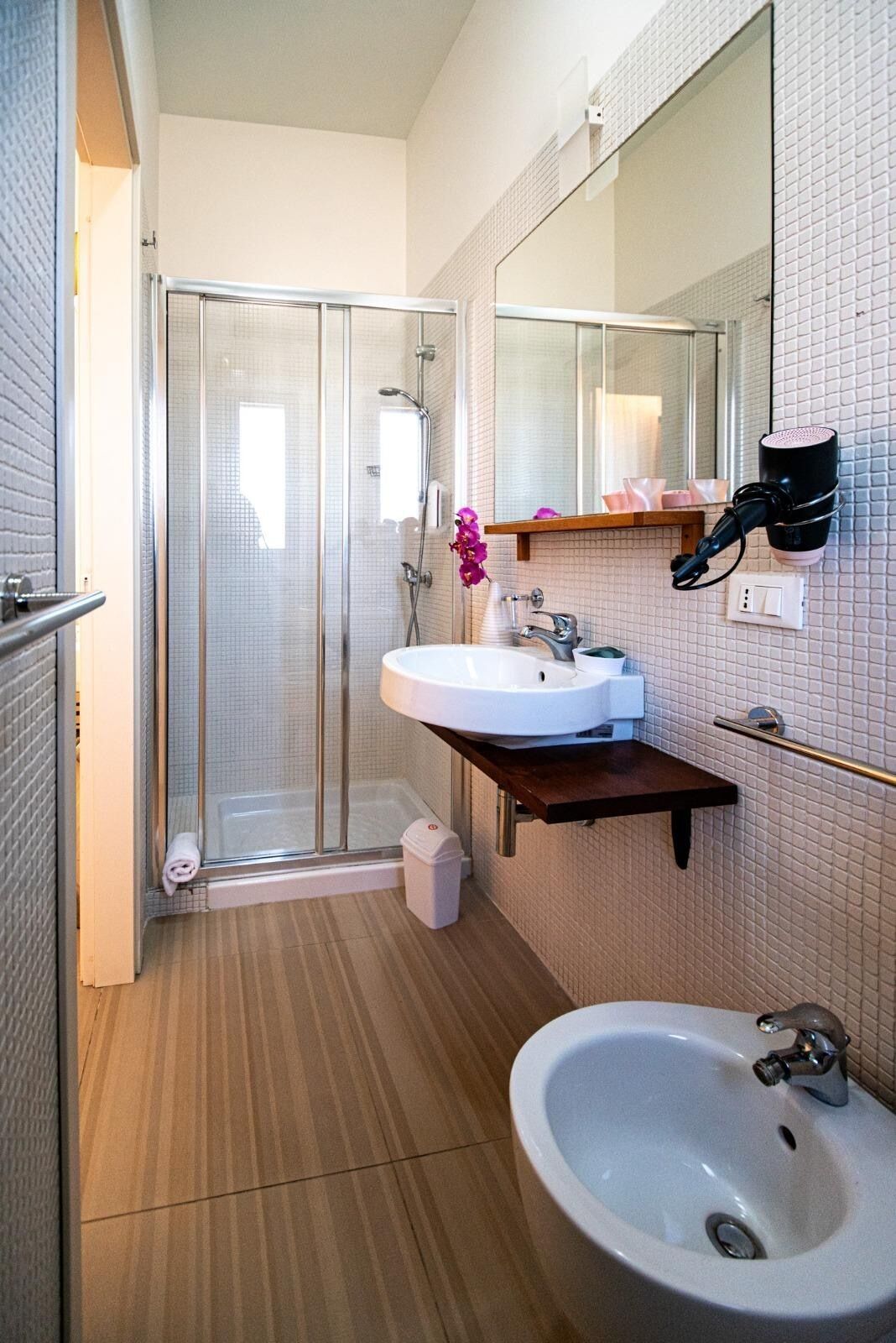 A bathroom with a glass shower enclosure, a white sink, a bidet, and a mirror.