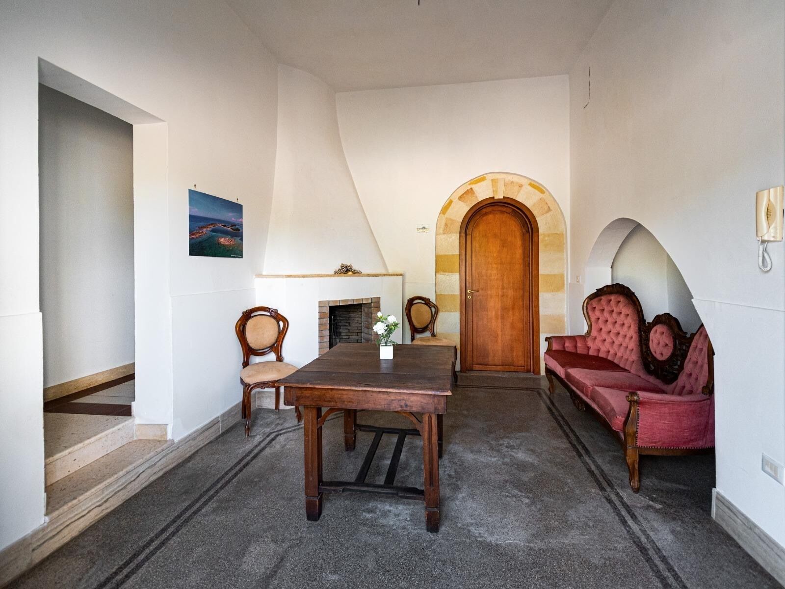Um quarto com uma mesa de madeira, um sofá, uma lareira e uma porta em arco.