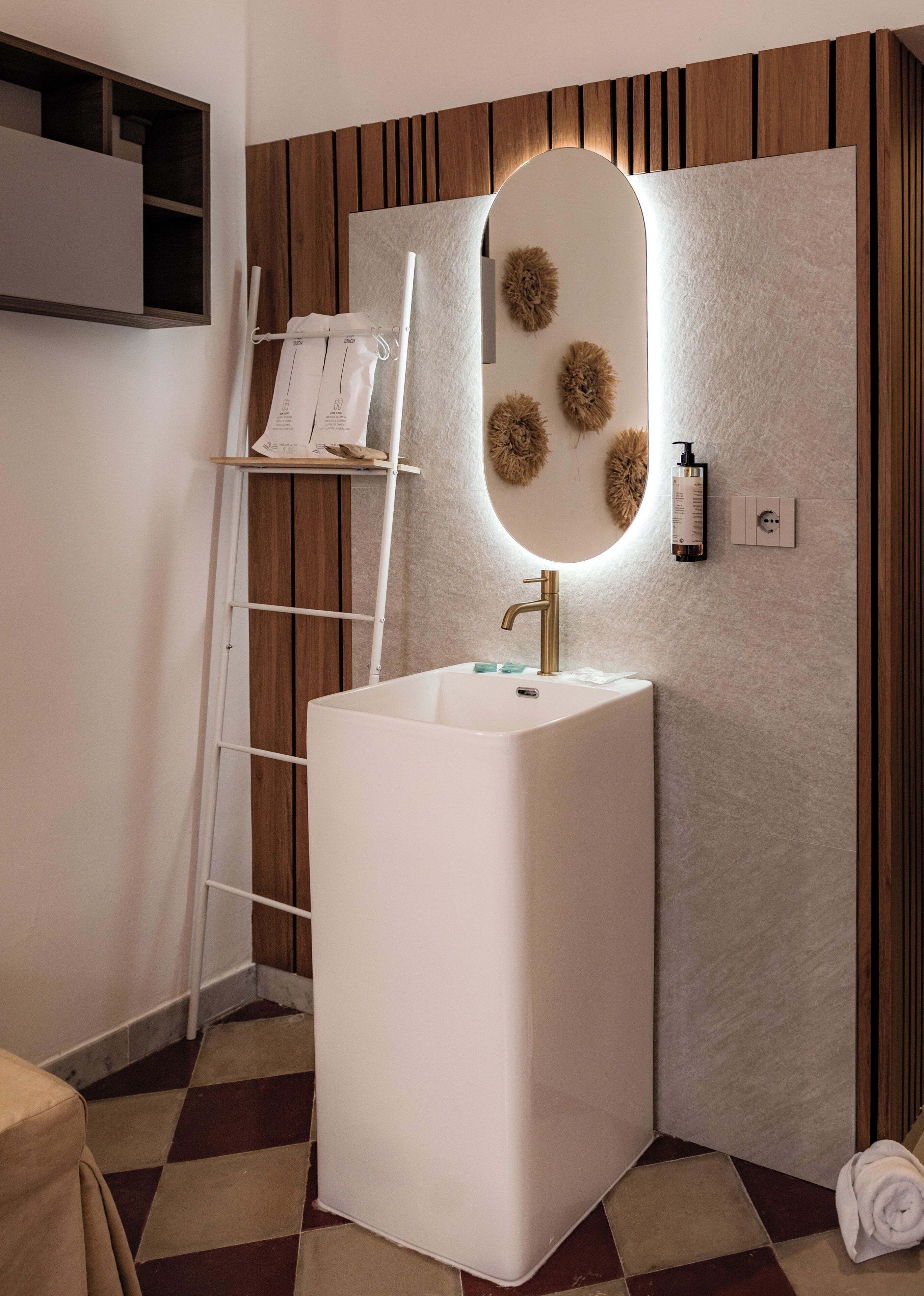 Un baño con un lavamanos pedestal blanco, un espejo con marco de madera y una toalla en el suelo.