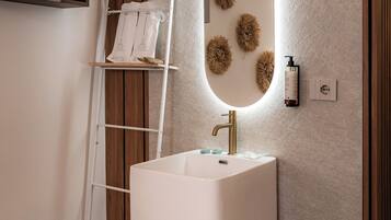 Un baño con un lavamanos pedestal blanco, un espejo con marco de madera y una toalla en el suelo.