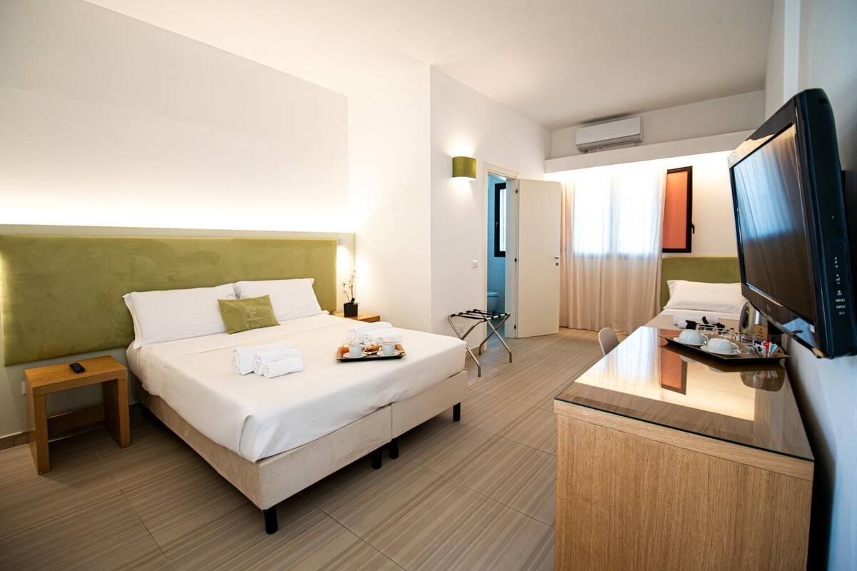 A hotel room with a bed, bedside table, TV, and a desk with breakfast items.