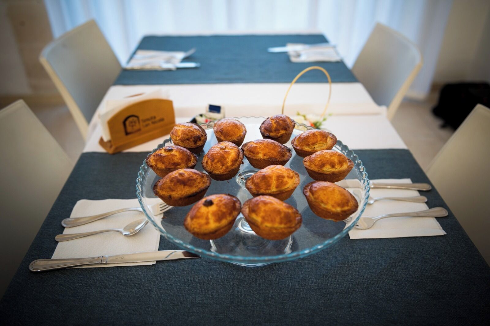 Una mesa con una fuente de pasteles, un letrero con un logotipo y cubiertos.