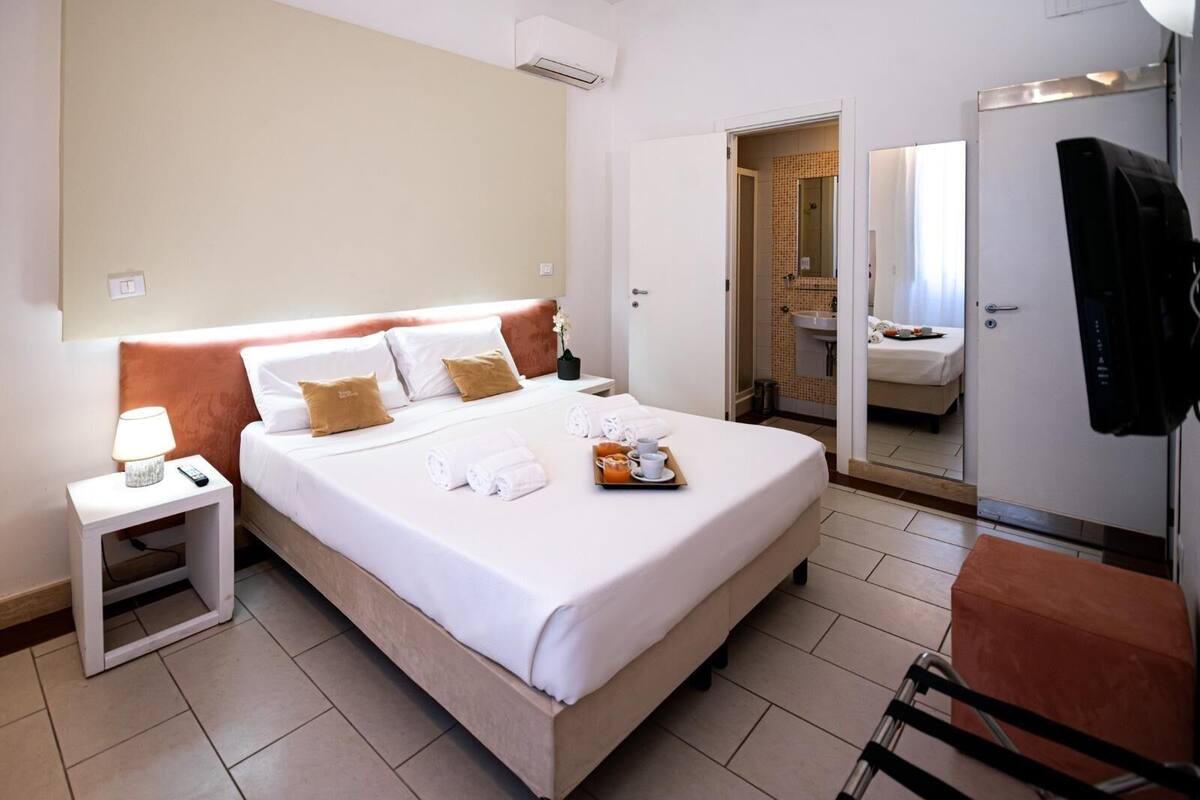 A hotel room with a bed, bedside table, lamp, and a bathroom visible through an open door.
