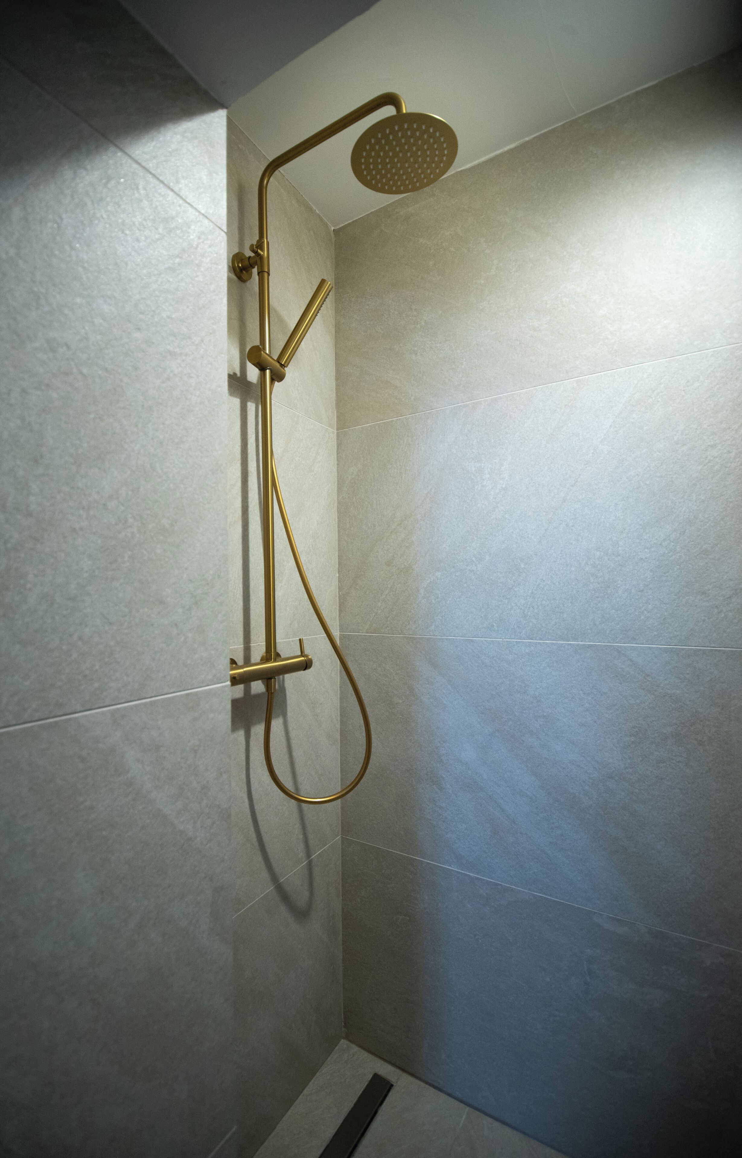 Ducha con cabezal y manguera dorados, frente a una pared de azulejos.