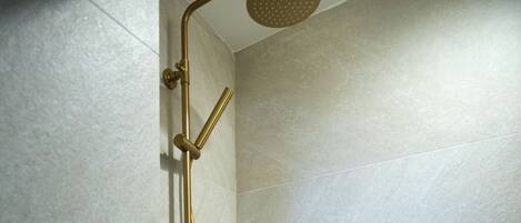 Ducha con cabezal y manguera dorados, frente a una pared de azulejos.