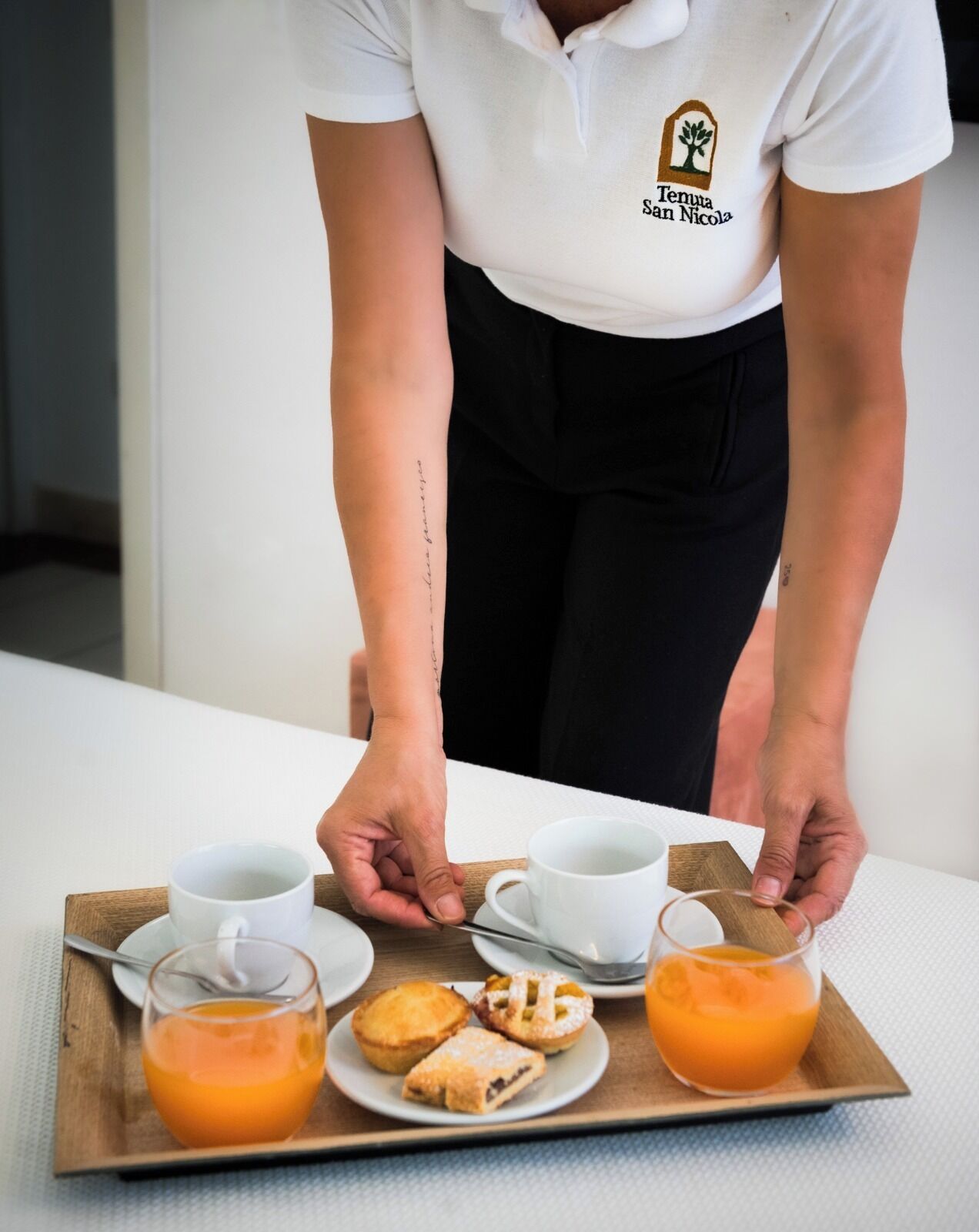 Eine Person serviert ein Tablett mit Getränken, Gebäck und einer Tasse.