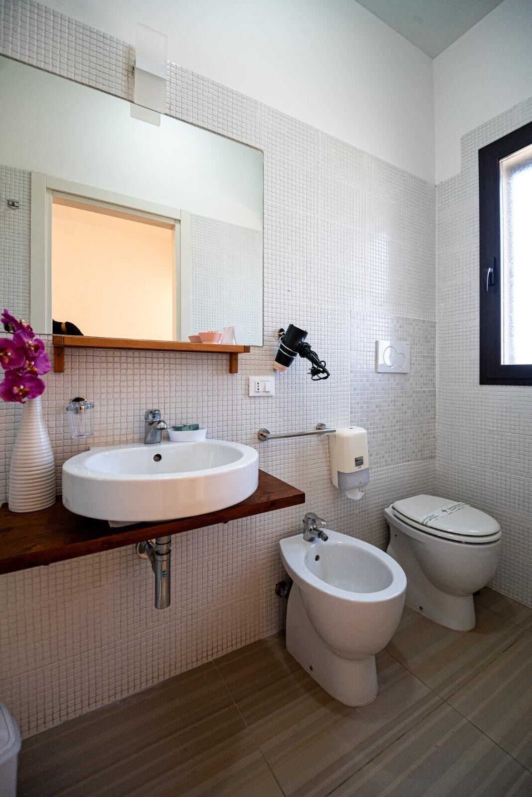 A bathroom with a large mirror, two sinks, a bidet, and a toilet.