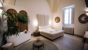 A bedroom with a bed, bedside table, round rug, potted plant, and a large mirror. - Tenuta San Nicola (Novoli)