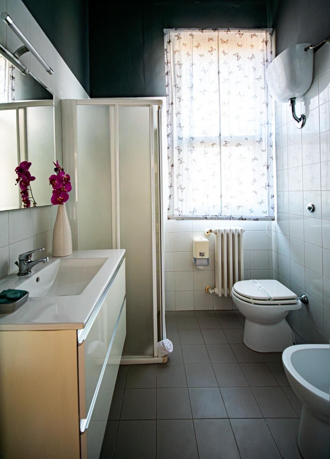 A bathroom with a shower, toilet, sink, and a window with patterned curtains.