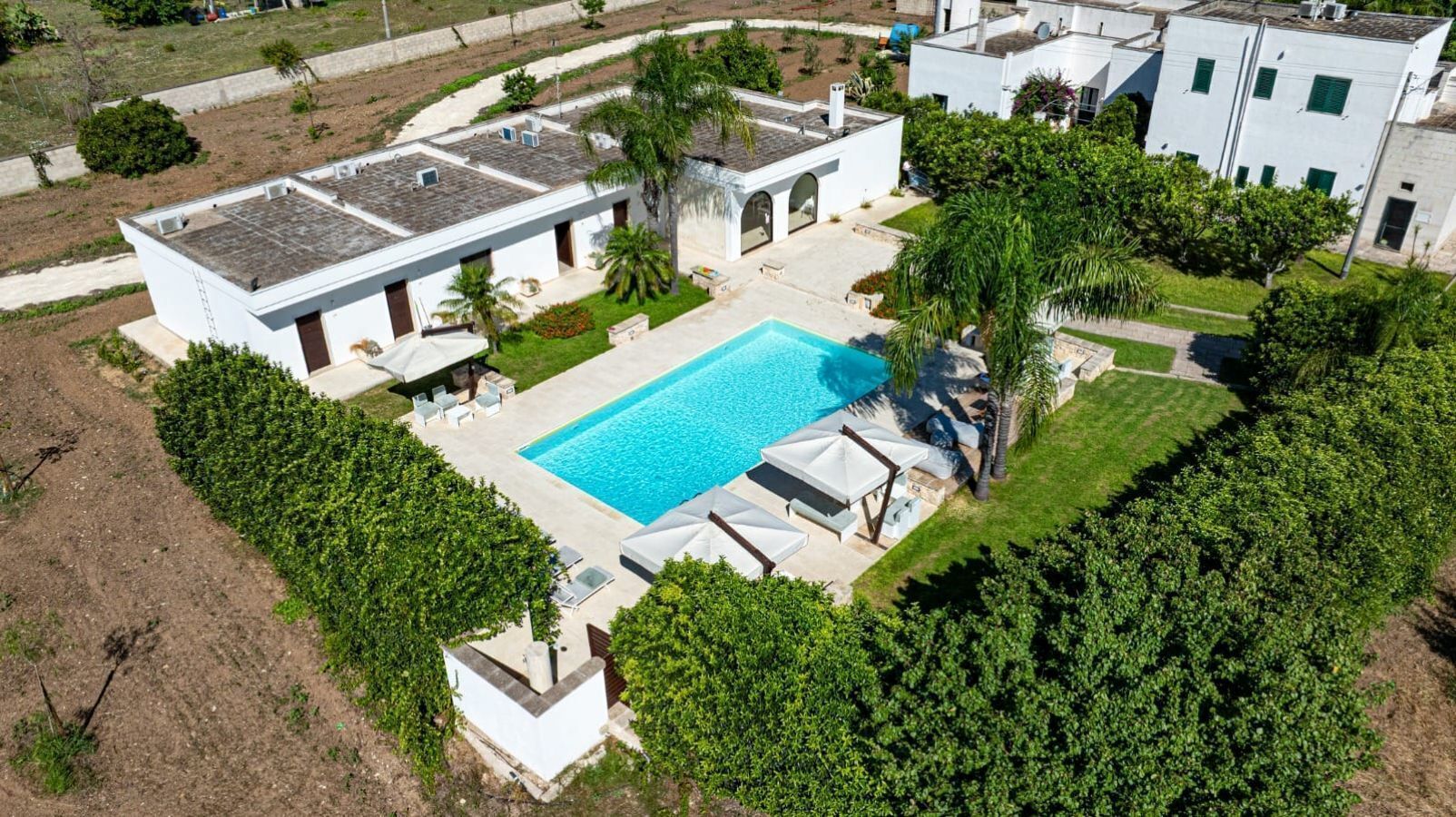 A residential property with a swimming pool, white buildings, and lush greenery.