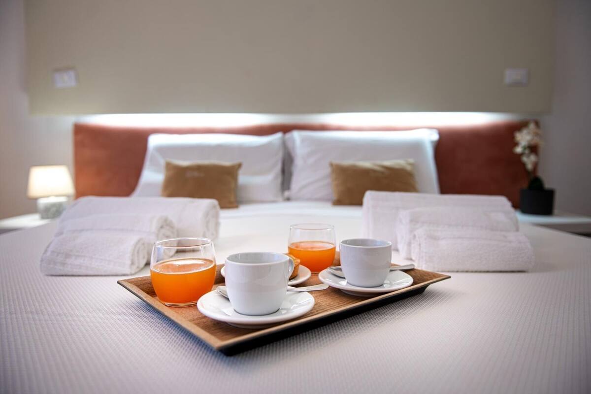 A neatly made bed with white linens, two pillows, and a tray with two glasses of orange juice and two white cups.