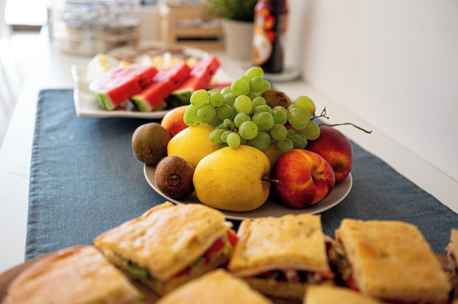 Un plato con frutas variadas y sándwiches sobre una mesa.