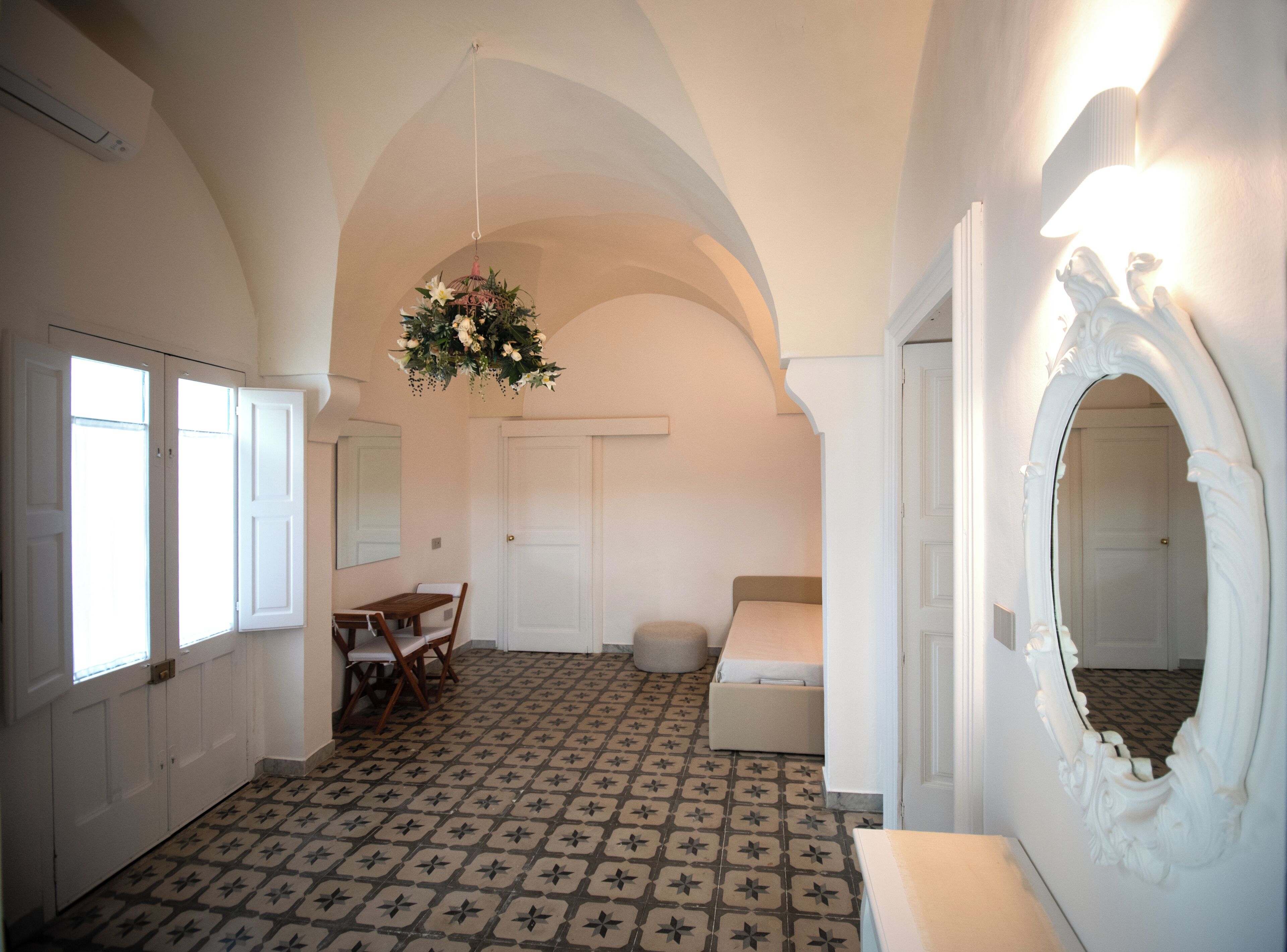 A room with a patterned floor, a dining table with chairs, a hanging floral arrangement, and a mirror with an ornate frame.