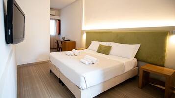 Ein Hotelzimmer mit Bett, Nachttisch, einem an der Wand befestigten Fernseher und einem Schreibtisch mit Stuhl.