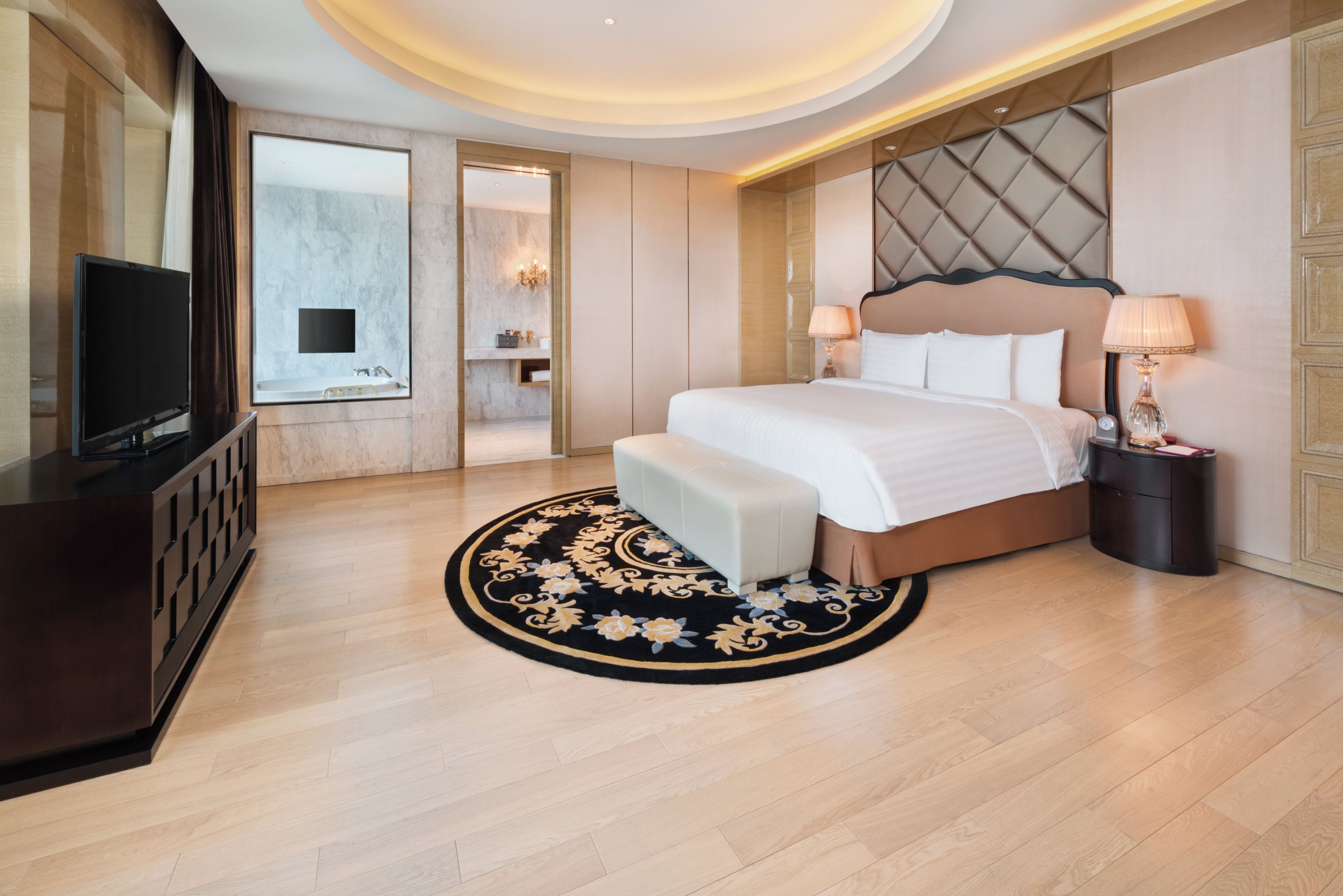 A hotel room with a bed, bedside lamps, a TV, a bathroom with a mirror, and a wooden floor.