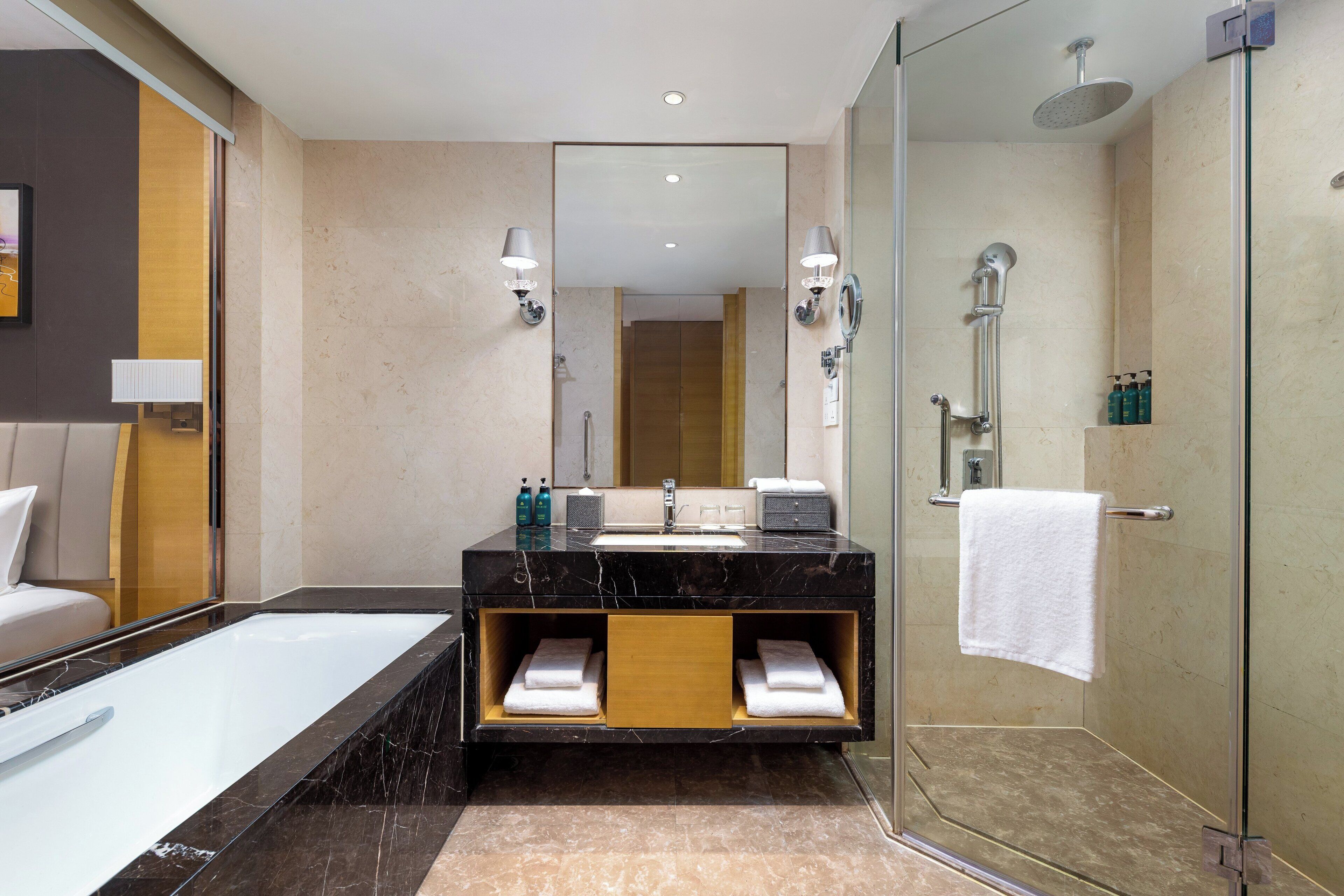 Ein modernes Badezimmer mit einer Glaskabine zur Dusche, einem großen Spiegel und einem schwarzen Marmorwaschbecken.