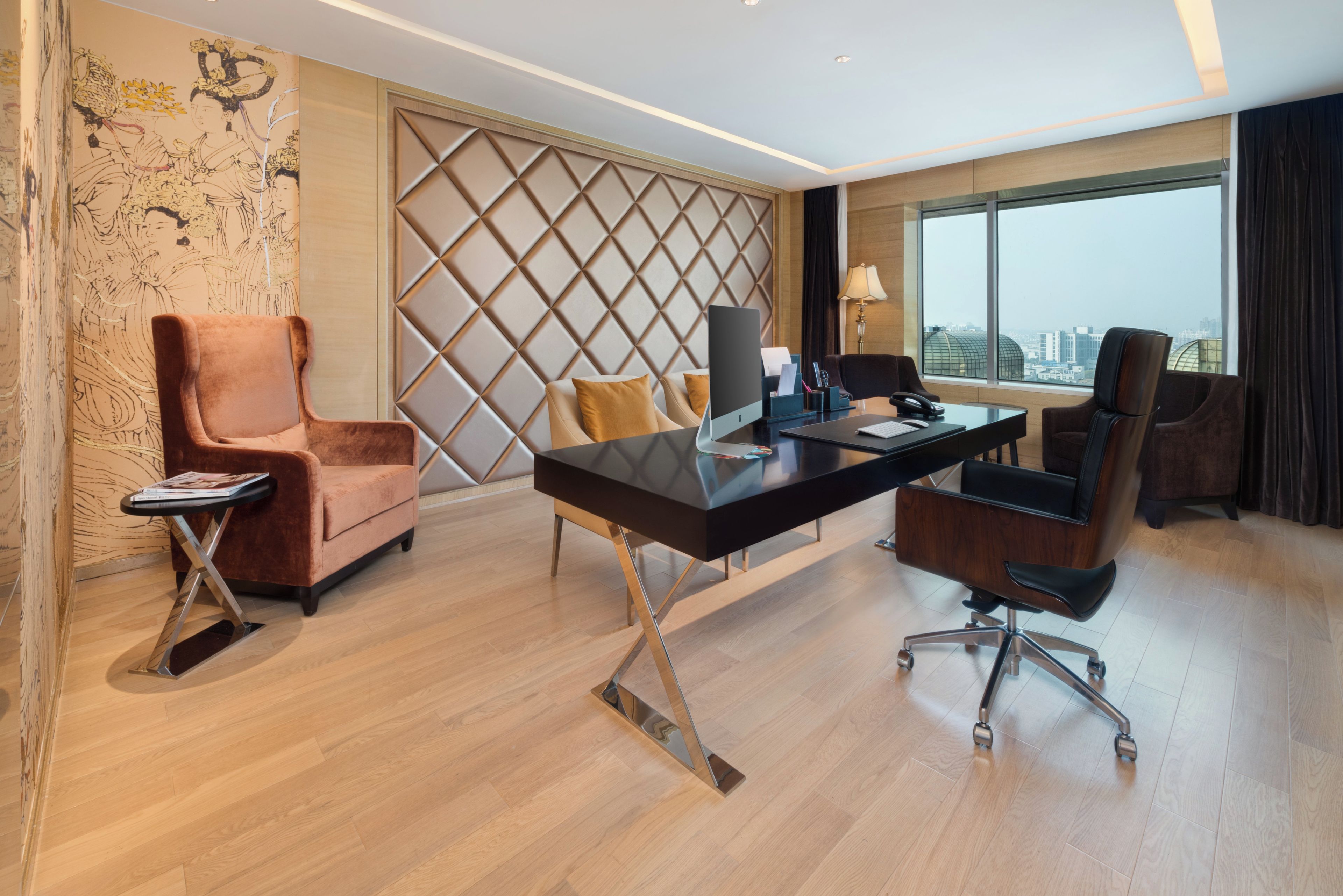 Une chambre d’hôtel moderne, dotée d’un grand bureau, de deux chaises, d’un ordinateur portable et offrant une vue sur la ville.