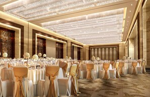 A banquet hall with round tables, chairs, and floral centerpieces.