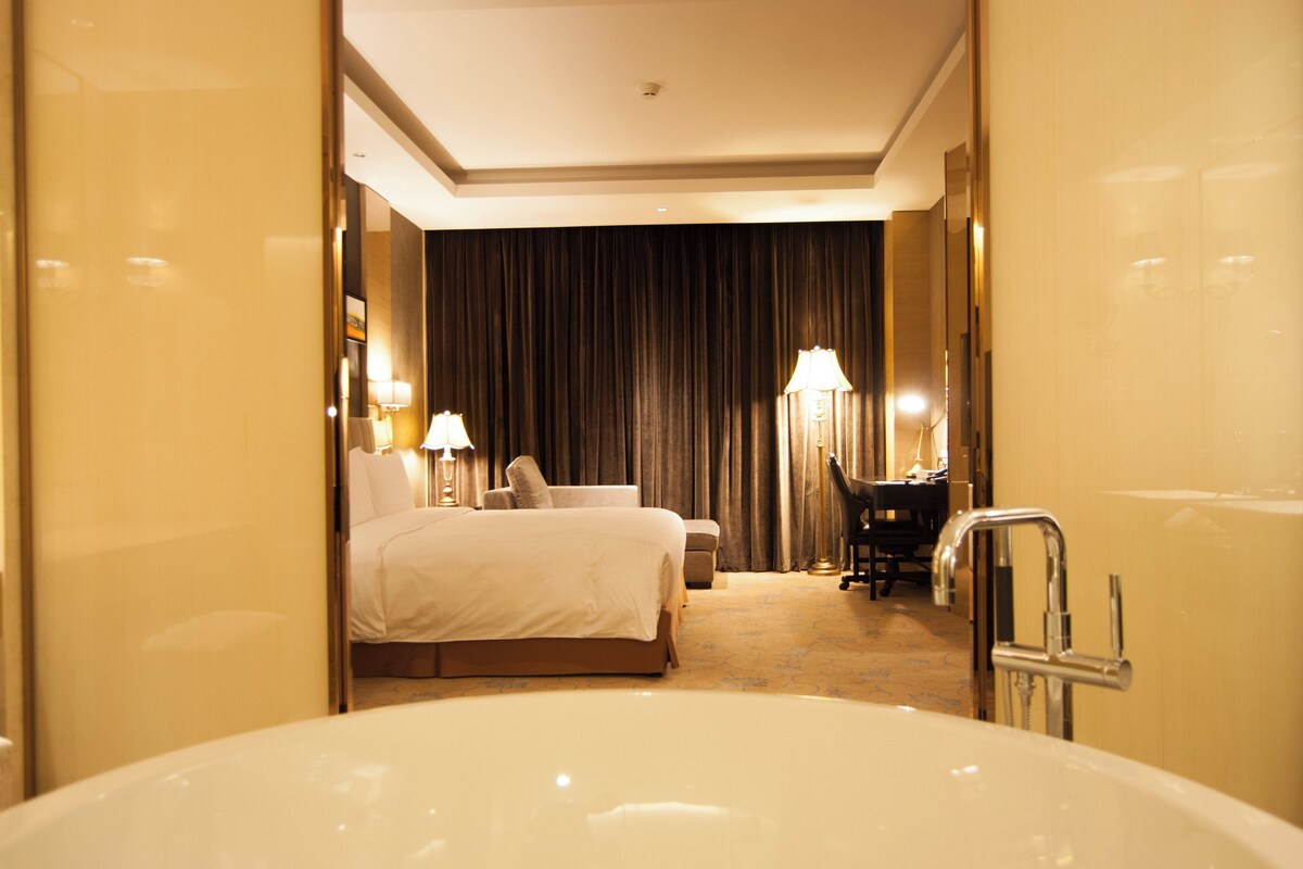 A hotel room with a large bathtub, a bed, a desk, and a chair.