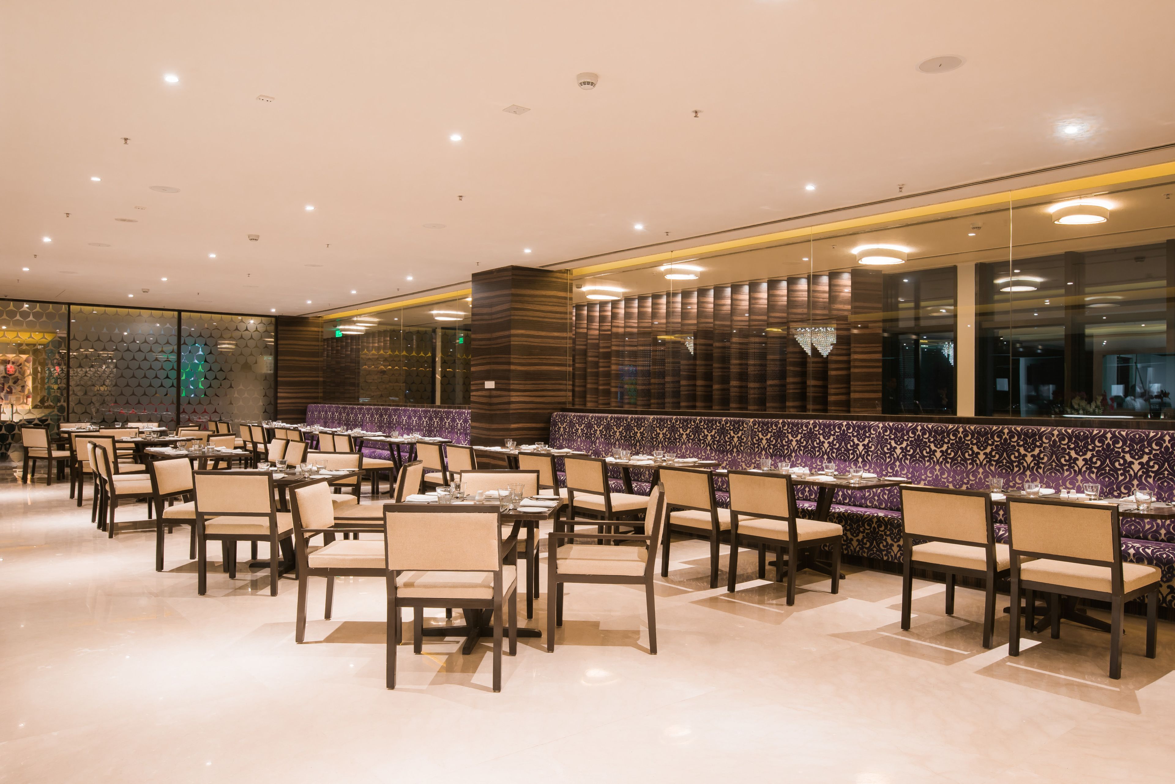 A spacious restaurant with multiple tables and chairs, a patterned wall, and a modern ceiling design.