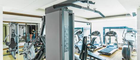 Un gimnasio con equipo de ejercicio, espejos y una cinta de correr.