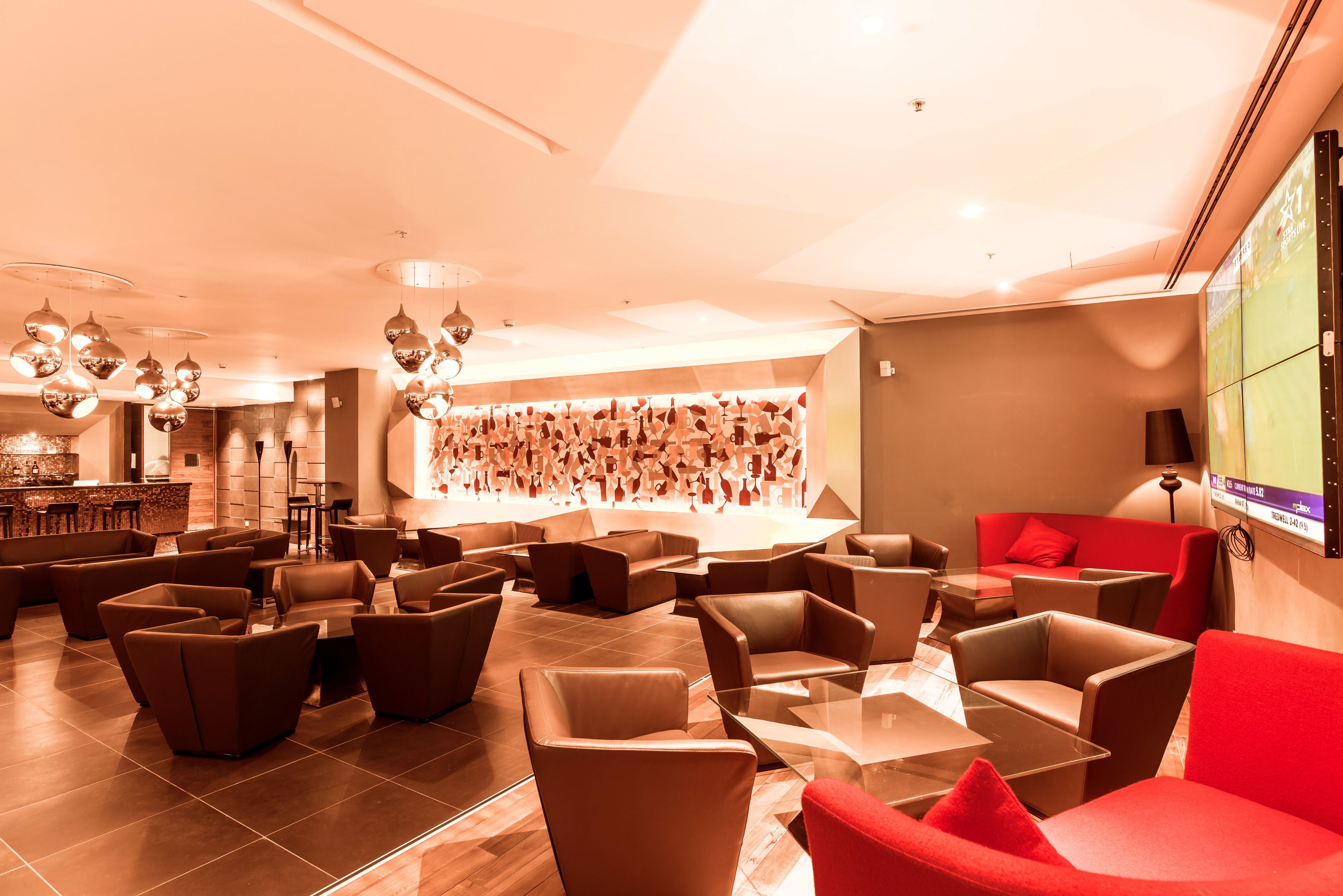 A modern lounge area with multiple seating options, a bar, and a large screen displaying content.