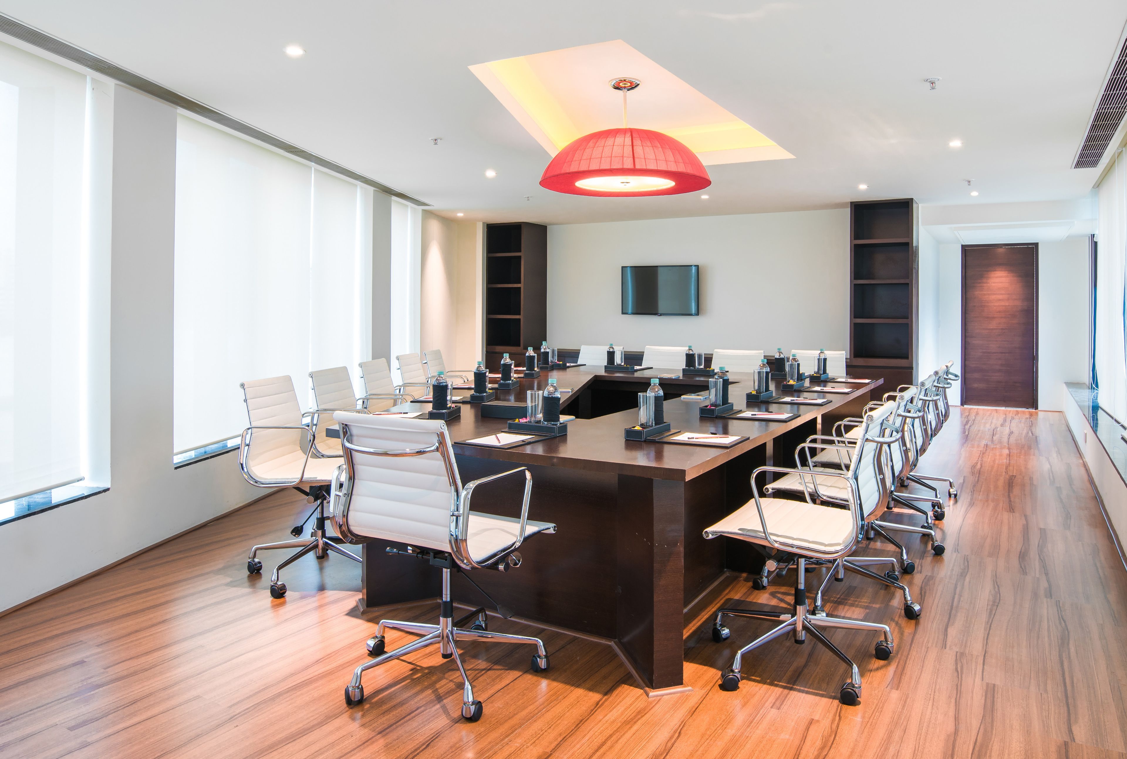 A conference room with a long table, chairs, a TV, and a red pendant light.