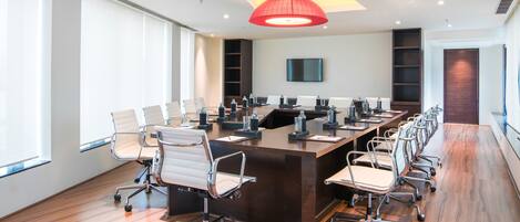 Un salón de conferencias con una larga mesa, sillas, un televisor y una lámpara colgante roja.