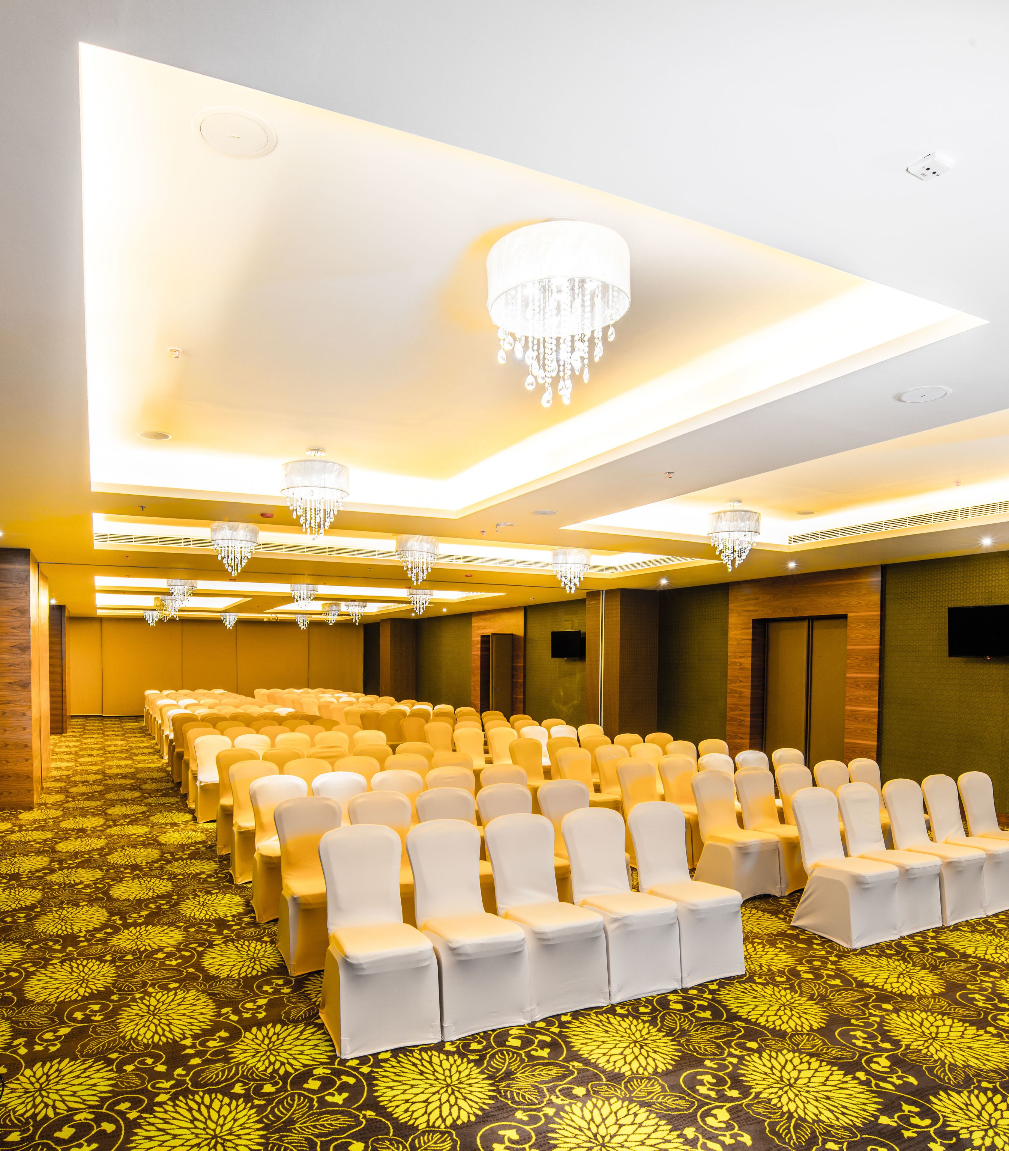 Une salle de conférence avec des rangées de chaises blanches, des lustres et une moquette à motifs.
