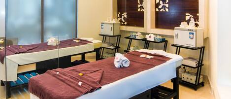 Une salle de spa moderne équipée d’une table de massage, d’un petit coin salon et d’une coiffeuse avec un miroir et des rangements.