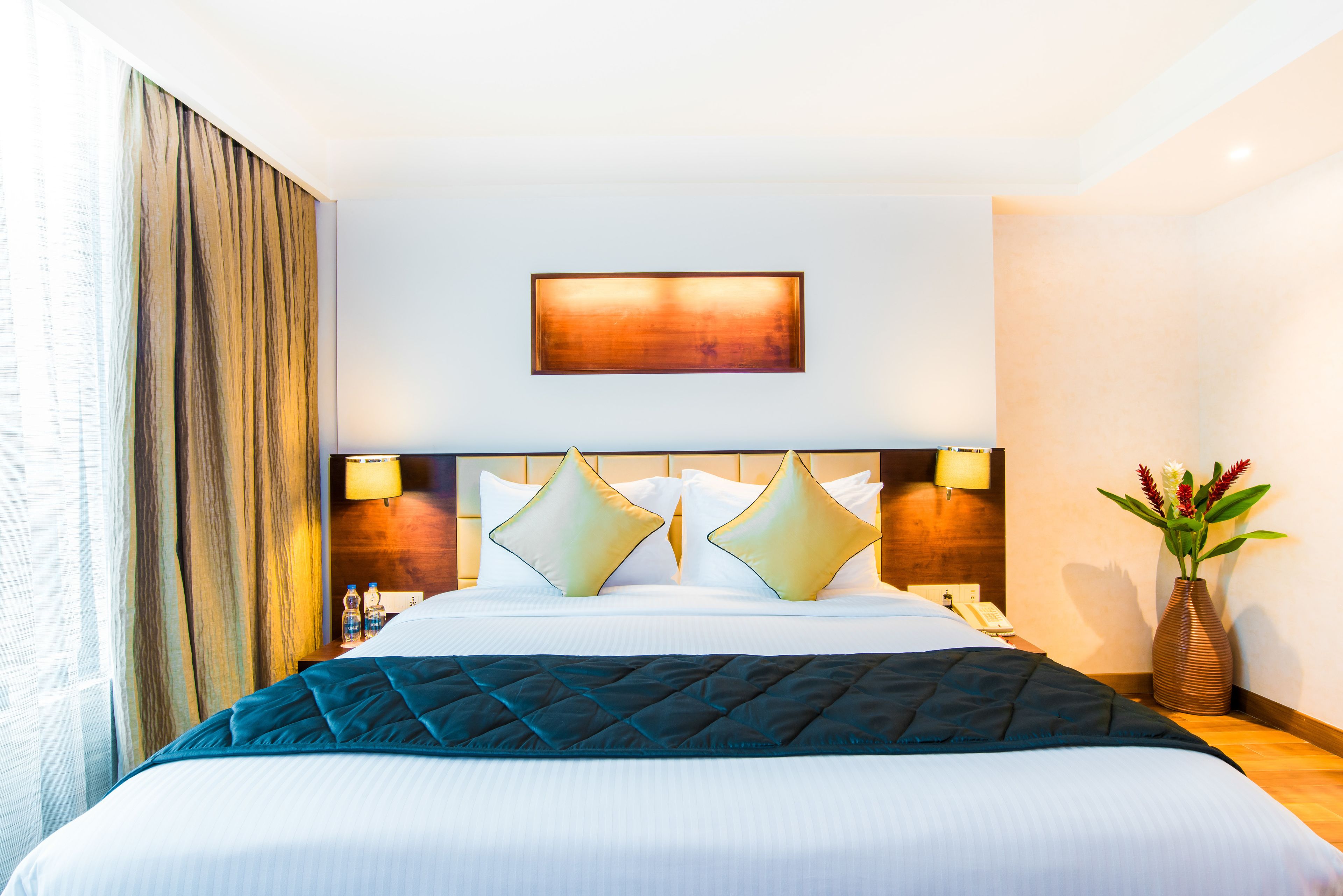 Hotelkamer met een groot bed, twee bedlampen, een nachtkastje, een vaas met bloemen en een schilderij aan de muur.