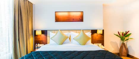Una habitación de hotel con una cama grande, dos lámparas de noche, una mesita de noche, un florero con flores y un cuadro en la pared.