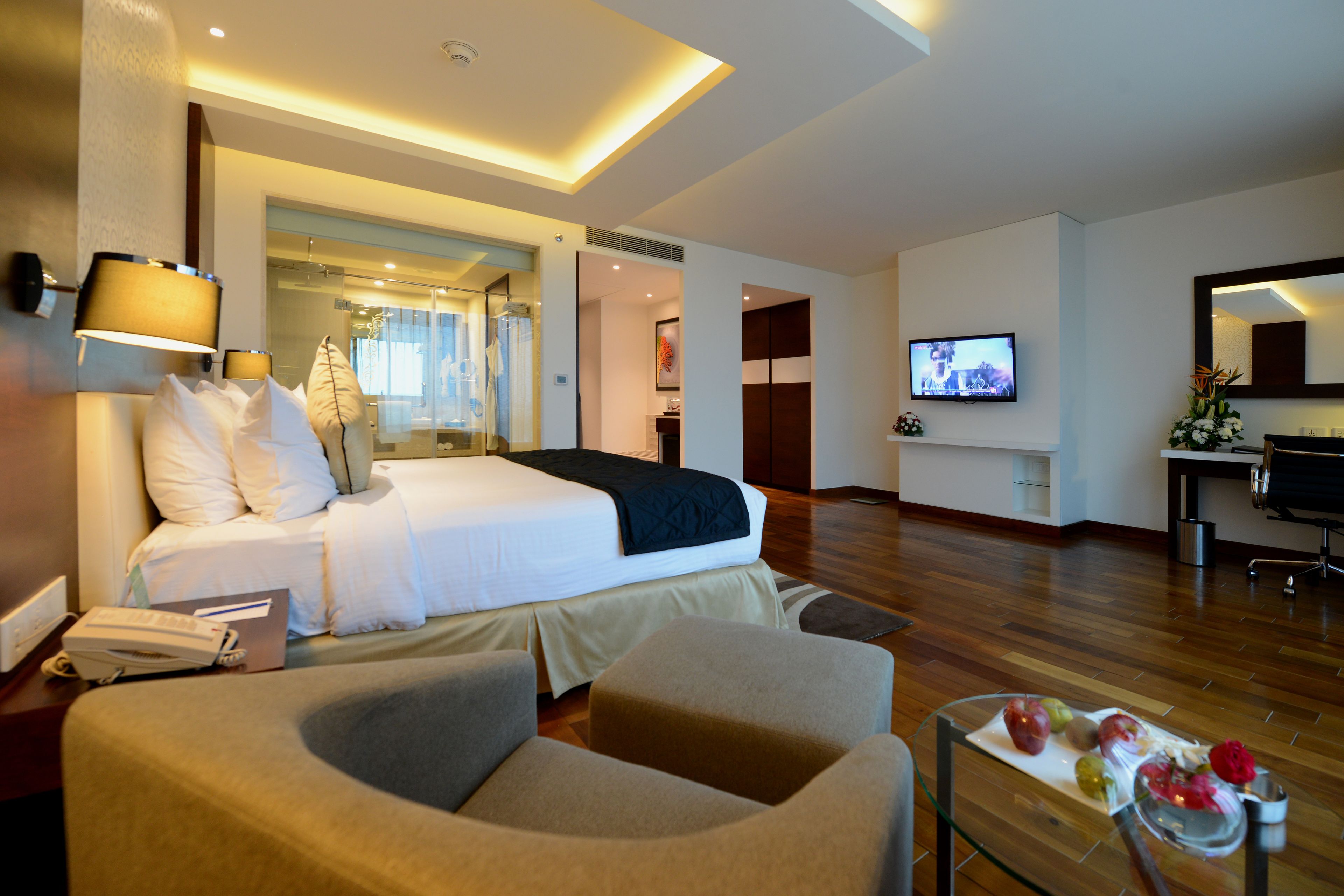 A hotel room with a bed, a desk, a TV, and a dining area with fruit.