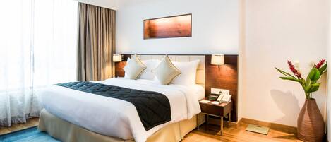 A hotel room with a large bed, bedside tables, a nightstand, a vase with flowers, and a painting on the wall.