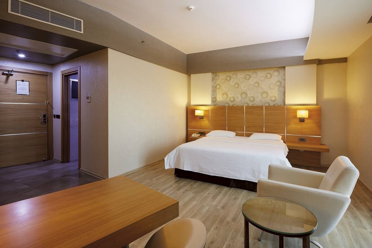 A hotel room with a bed, bedside tables, a desk, a chair, and a small table.