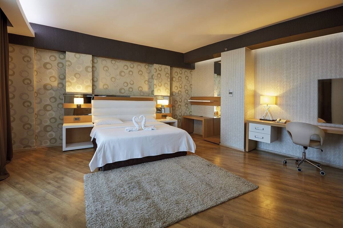 A hotel room with a bed, bedside tables, a desk, a chair, and a large mirror.