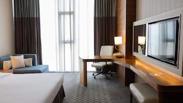 Una habitación de hotel con una cama, un escritorio con una silla, un televisor y un sofá.