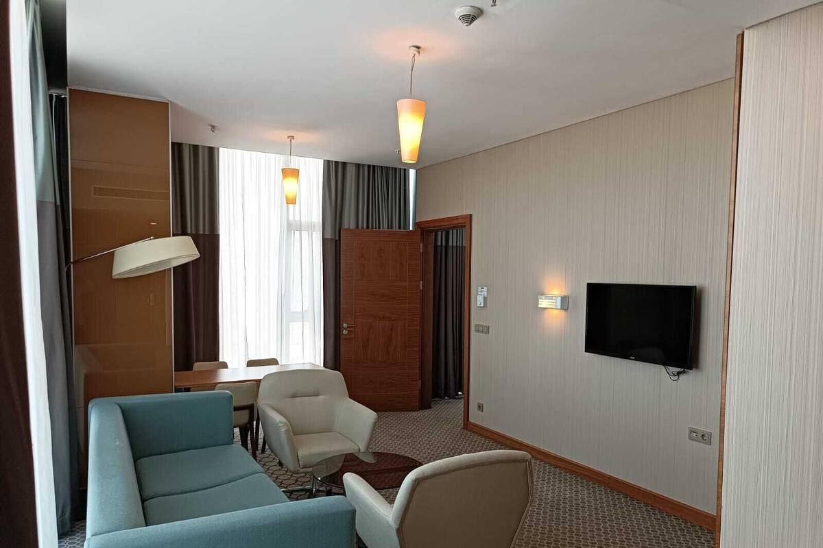Une chambre d’hôtel avec un canapé, deux fauteuils, une petite table, un téléviseur et une lampe.